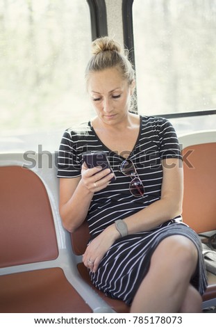 Beautiful middle aged adult woman checking her cell phone while riding a bus or training during a busy day. She is checking social media or her email while traveling