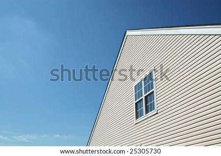 Side of new house showing peaked roof and blue sky. Pair of double-hung windows.