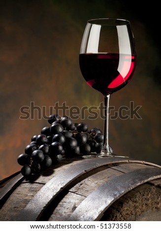 glass of red wine with grapes and old barrel