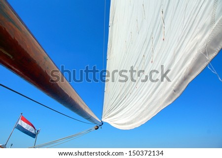 white sail against a blue sky on a old wooden sailboat. In the corner a dutch flag