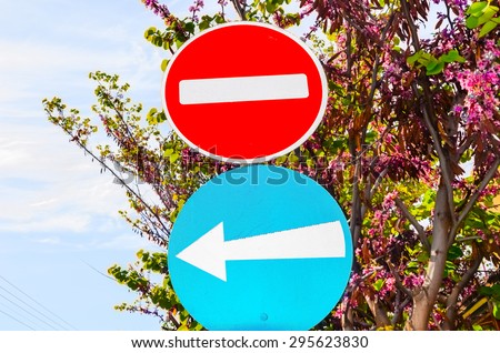 Traffic sign prohibited direction  and mandatory sense blue arrow direction on blue sky Cyprus and Judas tree.