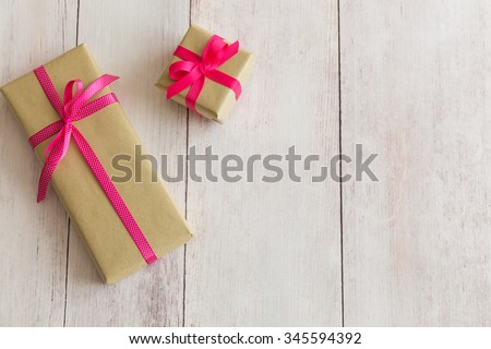 Two presents gifts boxes with brown wrapping paper and pink and pink and white polka dot ribbons on off white wooden background