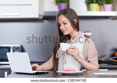 Young woman at home in the kitchen and looking at the computer