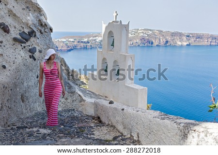 Woman walks up the mountain stairs, at the bottom of the bell tower of the Church. Greece Santorini