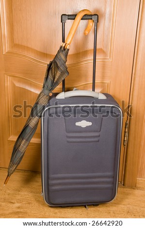 Suitcase and umbrella of green color against a wooden door.