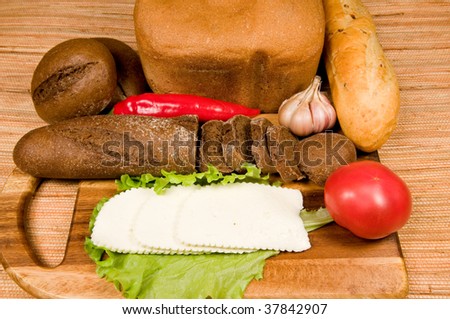 The cut white cheese, bread and vegetables on   wooden board.