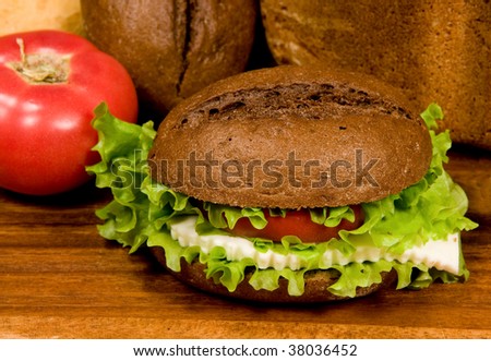 Sandwich with rye bread cheese and vegetables on a wooden board.