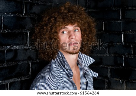 Portrait young man with a curly hair against a black wall