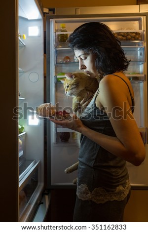 Woman and cat at night looking for food in the fridge