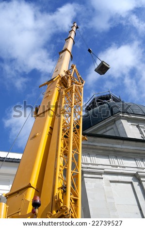 Yellow mobile crane hydraulic boom raises cargo against a blue sky