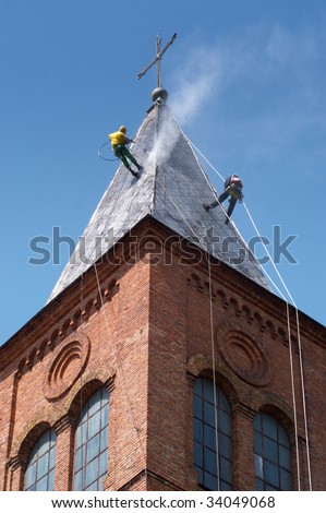 Two climbers on a dome of the church, carrying out works under pressure washing a roof