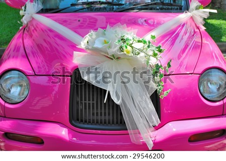 Pink, classic-styled wedding car with a bouquet of flowers attached to the sides and the bonnet.
