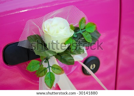 Pink, classic-styled wedding car with flower decoration attached to the car door