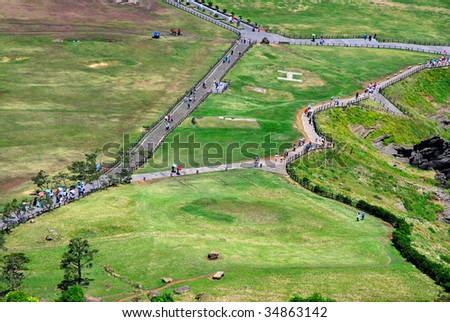 Bird\'s eye view of people strolling along the mountain paths with a helipad in the background