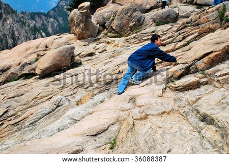 Young man climbing treacherous steep mountain cliff full of rocks and boulders. Symbol of strength and determination.