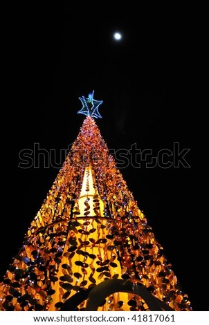Christmas tree lit up with decorations and colorful lights, on a full moon night. Suitable for winter seasons, christmas and holiday concepts.