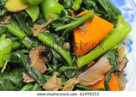 Sumptuous Chinese vegetarian cuisine. Ingredients include green, leafy vegetables, mushrooms, carrots, and slices of ginger.