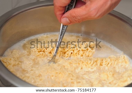 Hand cooking and stirring noodles in cooking pot of boiling water.