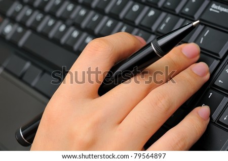 Hand holding business pen and typing on new black keyboard.