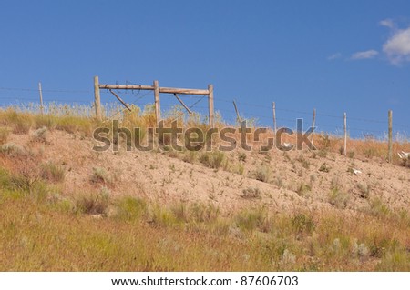 Wooden gate with wired barb wire fence with blue sky background.