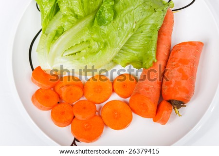 Well-cut carrots and green vegetable on a white porcelain dish on a white background
