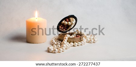 pearl beads, a box of rouge and white round burning candle  on a light background