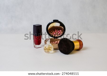 perfume in a transparent bottle, red nail polish and rouge on a light background