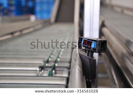 Close up shot of a roller conveyor with a laser distance sensor on the side. Photo taken in a big warehouse.