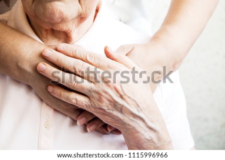 Mature female in elderly care facility gets help from hospital personnel nurse. Senior woman, aged wrinkled skin & hands of her care giver. Grand mother everyday life. Background, copy space, close up