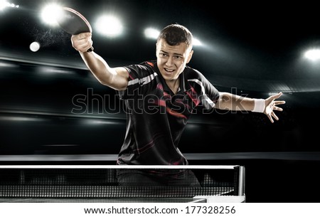 young sports man tennis-player in play on black background with lights