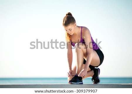 Young female runner is tying her running shoes on the ground