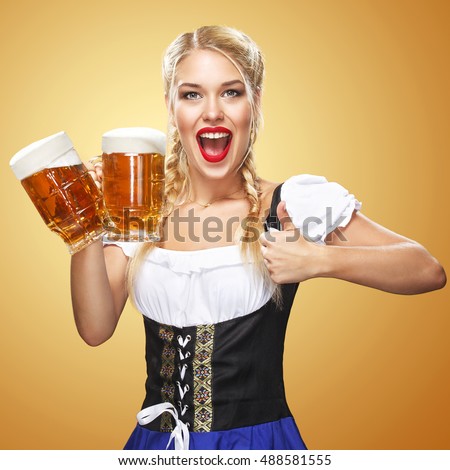 Young sexy Oktoberfest waitress, wearing a traditional Bavarian dress, serving big beer mugs on blue background. Thumbsup