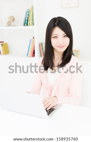young asian woman using laptop behind book shelf