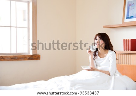 attractive asian woman drinking a cup of tea on the bed