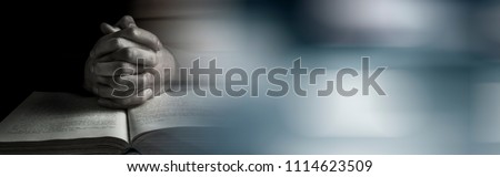 Hands of praying young man and Bible on a wooden desk background