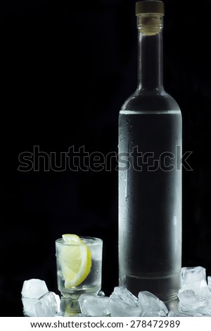 Close-up view of bottle of vodka with glasses standing on ice on black
