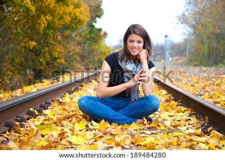A beautiful young woman sitting on a rail road track, surrounded by autumn leaves.