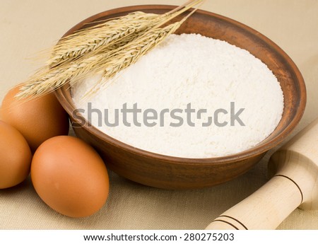 flour, egg, clay plate with flour and wheat ear on the tablecloth
