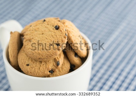 Close up of chocolate chip cookies or biscuit  in ceramic mug on blue table cloth