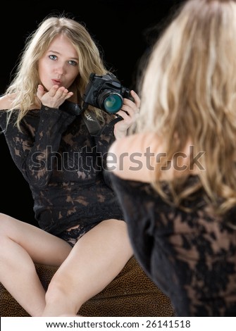 Young woman in sexy lingerie and holding a camera is blowing a kiss to her reflection in a mirror.