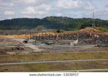 Earth-moving equipment at construction site. Men with survey equipment can be seen in foreground. Scene is at the Panama Canal, where a third set of locks are under construction.