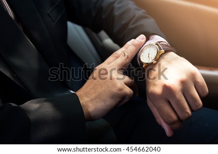 Businessman seats on the car and looking at watch ,business concept ,vintage tone