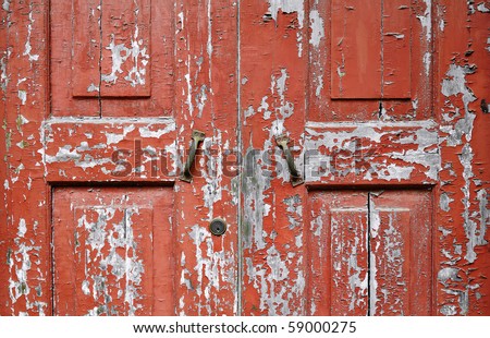 Peeling red-painted wooden door. Close-up shot showing weathered texture of paintwork.