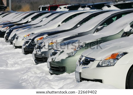 A row of cars covered in snow at a car dealership after a snow storm