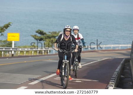 Two asian girl cycling uphill on the seafront road.