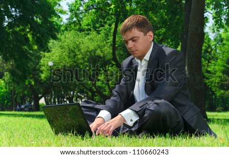 Young successful businessman resting in a park on the grass looking at the latest news on the Internet