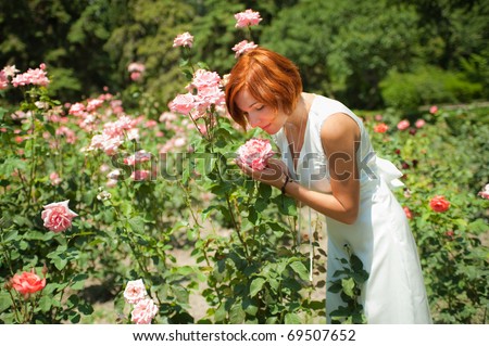 Beautiful young woman in a garden of roses at sunny summer day