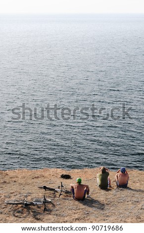Three men sitting on the beach looking into the distance beyond the horizon