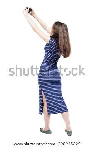 Back view of woman photographing.   girl photographer in dress. Rear view people collection.  Isolated over white background. Girl in a blue striped dress is photographed on a compact camera.