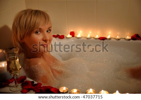 nude woman in foamy bath with petals of roses and by light of candles